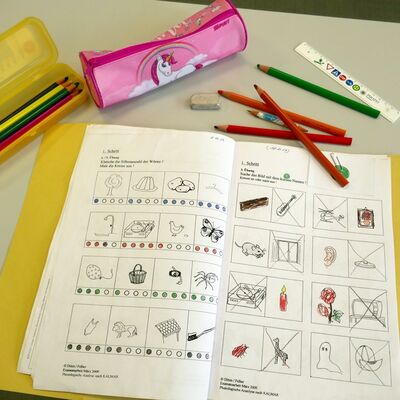 Arbeitsplatz einer Schülerin mit Arbeitsheft, Lineal, Radiergummi und verschiedenen Stiften