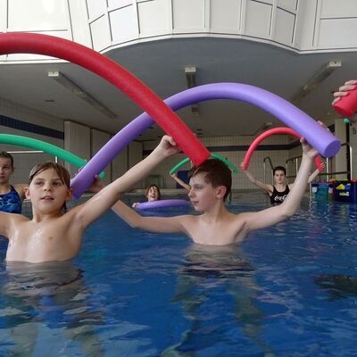 Schüler bewegen sich mit Schwimmnudeln im Therapiebecken